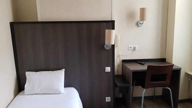 Une chambre d’hôtel équipée d’un lit, d’un bureau, d’une chaise, d’un téléphone et d’une lampe fixée au mur.