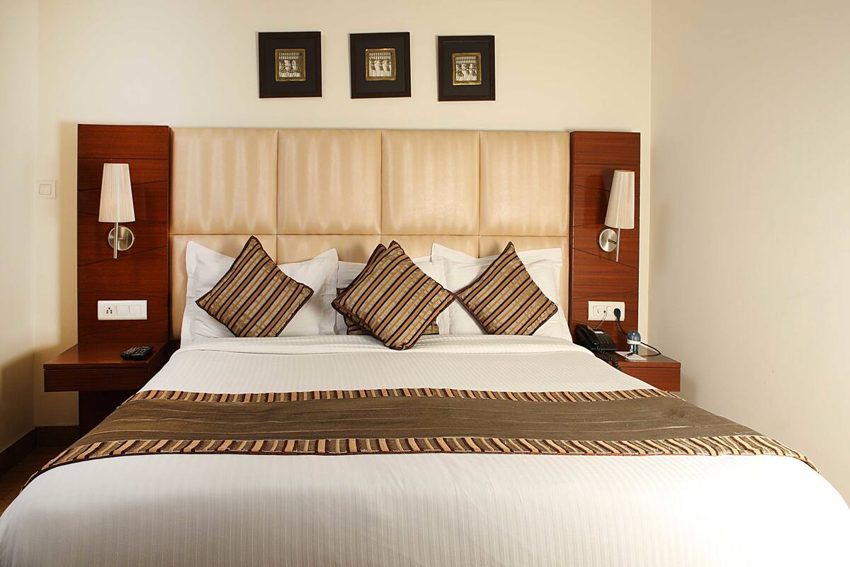 A hotel room with a large bed, two bedside tables, a headboard, and three framed pictures on the wall.