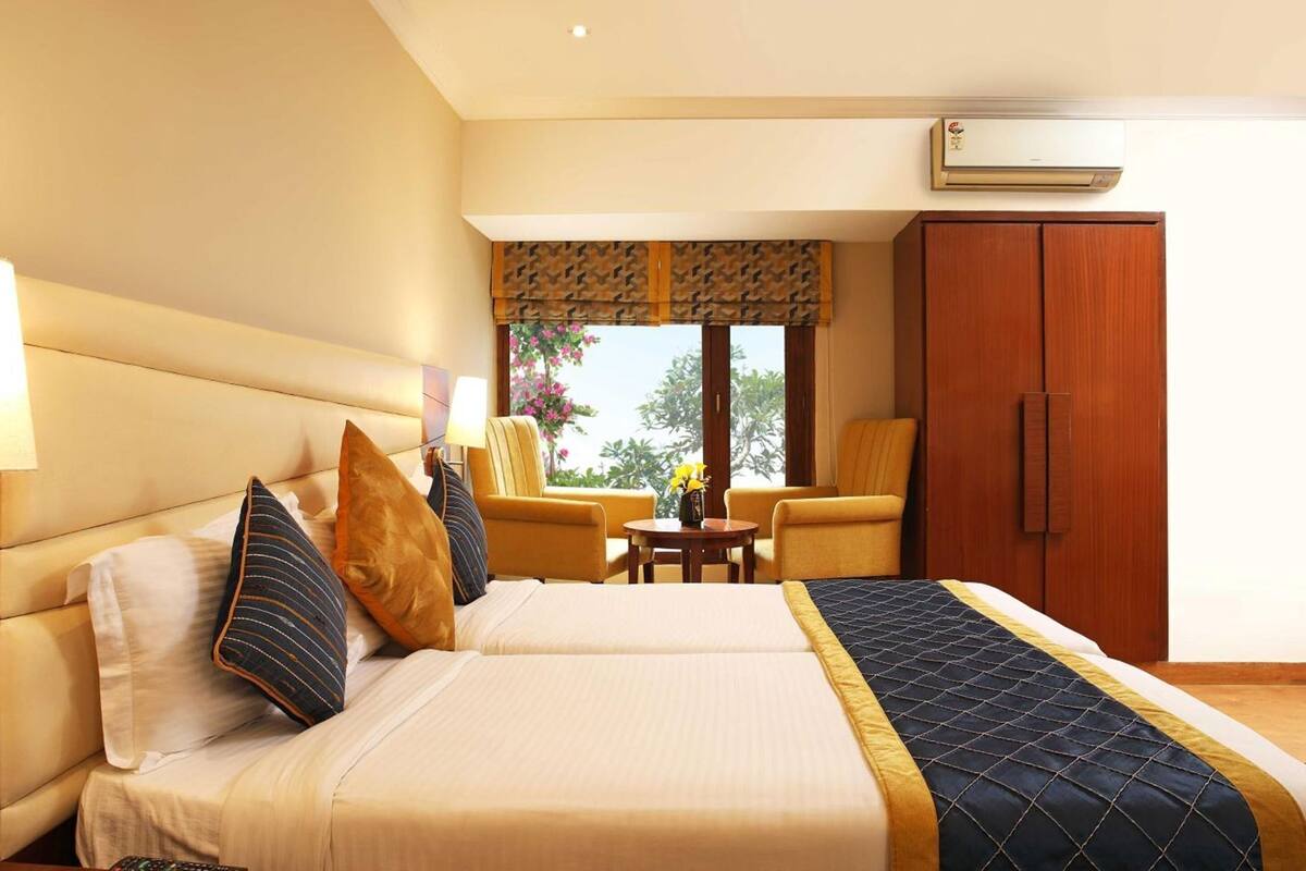 A hotel room with a bed, a desk, a chair, a wardrobe, and an air conditioning unit.