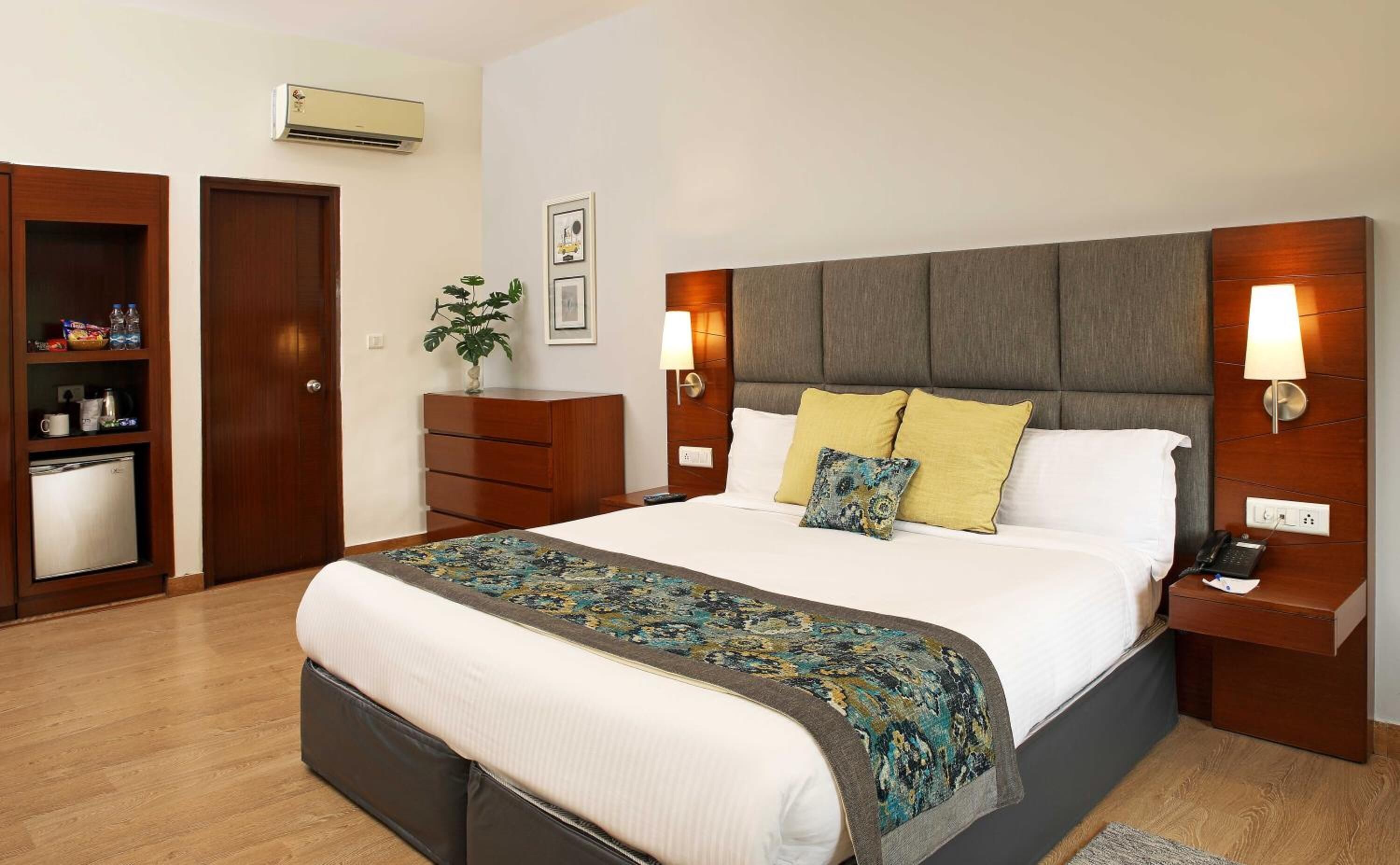 A hotel room with a large bed, bedside tables, a wardrobe, and a small kitchenette.