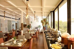 A dining area with tables set for breakfast, featuring a buffet with various food items and a view of the outdoors. - Ahuja Residency, Sunder Nagar (New Delhi)