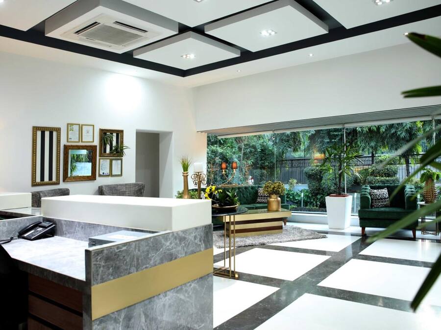 A modern reception area with a marble reception desk, framed certificates on the wall, and a view of a lush garden through large windows.