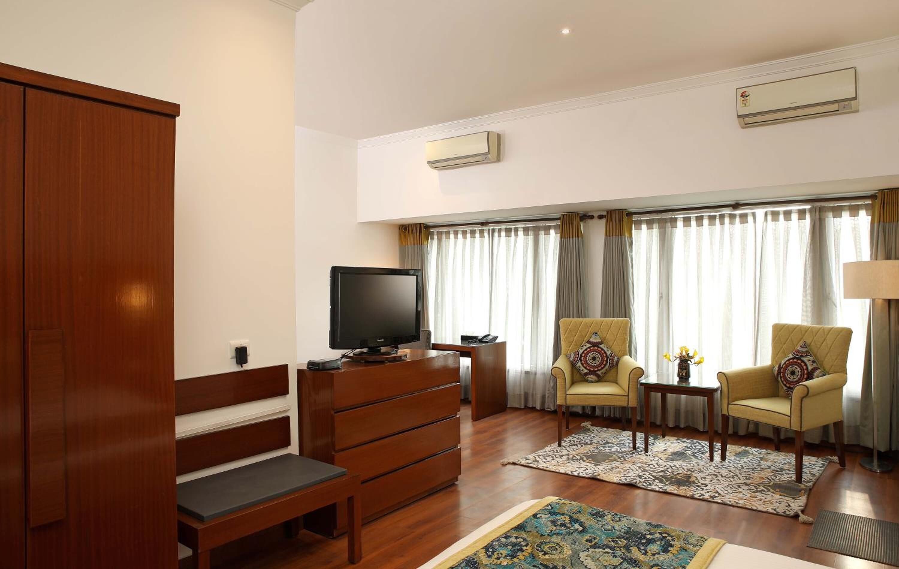 Un salón amplio con un banco de madera, un televisor, dos sillones, una mesita y un ventanal con cortinas.
