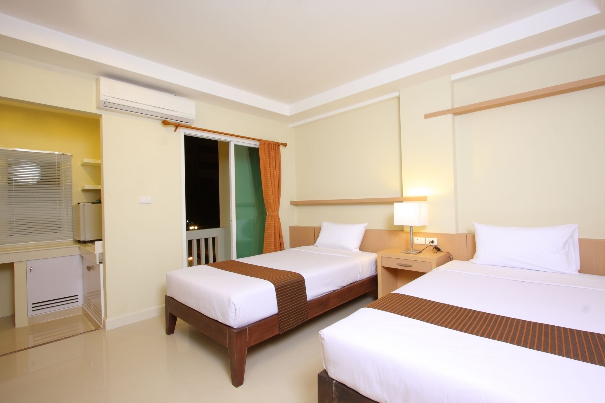 A hotel room with two beds, a desk, a television, and a window with curtains.