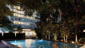 A swimming pool surrounded by palm trees and a building with illuminated windows at night.