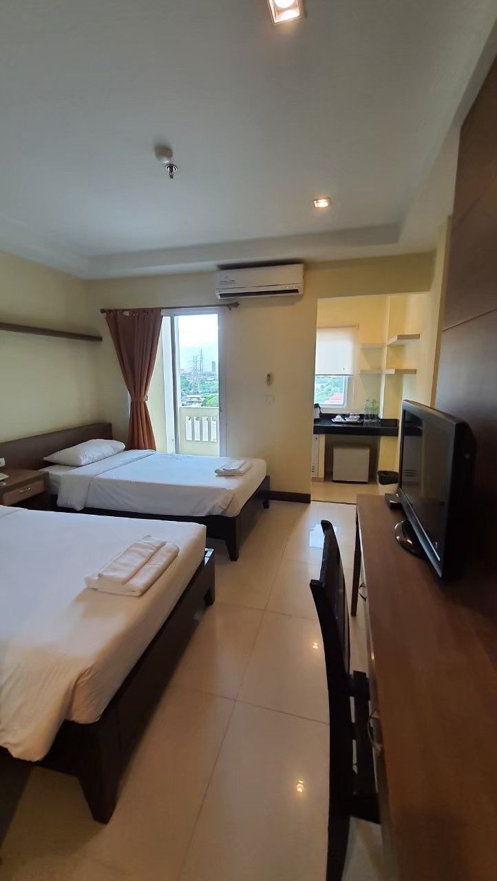 Habitación de hotel con dos camas, televisión, escritorio y kitchenette.