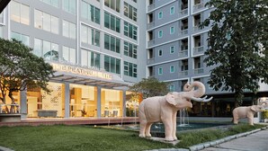 A modern building with a glass facade, a sign reading "The Platinum Suite," and two elephant statues in the courtyard. - Sunday Platinum Suites (Bangkok)