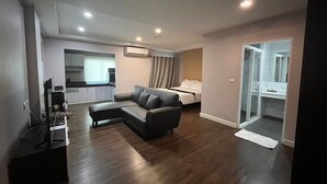 A modern living room with a sectional sofa, a bed, and a kitchenette in the background. - Sunday Platinum Suites (Bangkok)