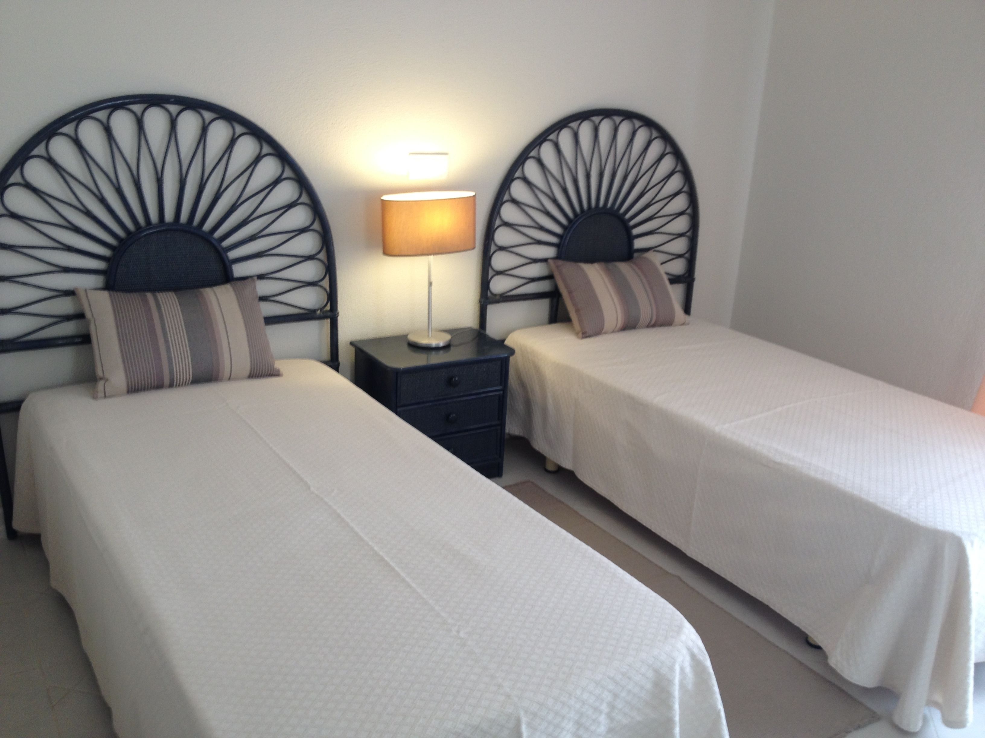 Two single beds with headboards, a bedside table, and a lamp between them.