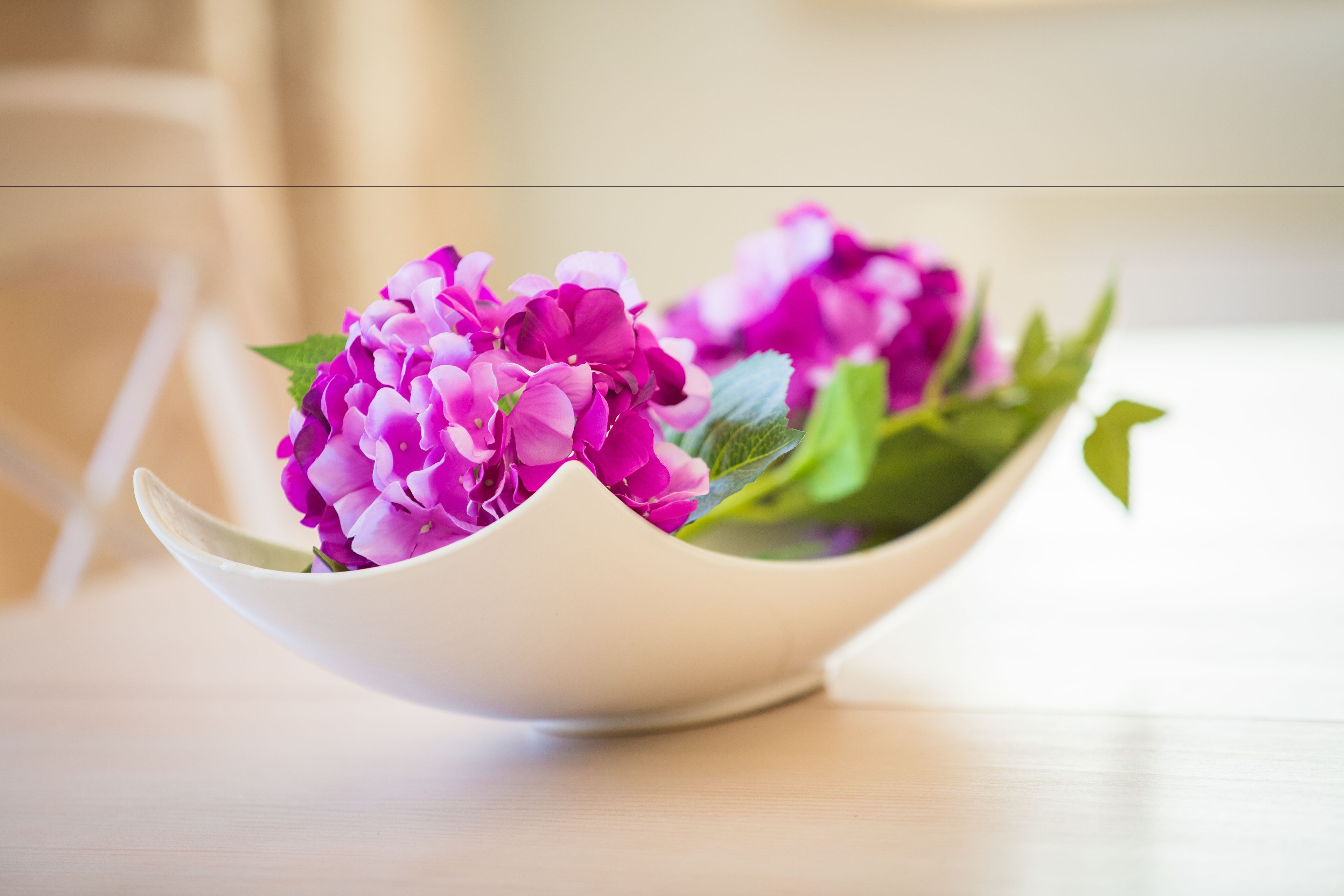 Een witte schaal met roze bloemen en groene bladeren op een houten ondergrond.