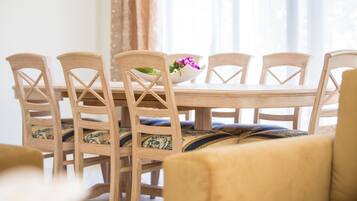 Et spisebord med seks træstole, en skål med blomster, og en sofa i forgrunden.