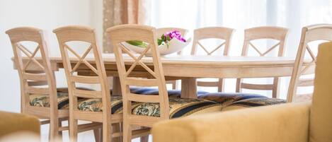 A dining table with six wooden chairs, a bowl with flowers, and a sofa in the foreground.