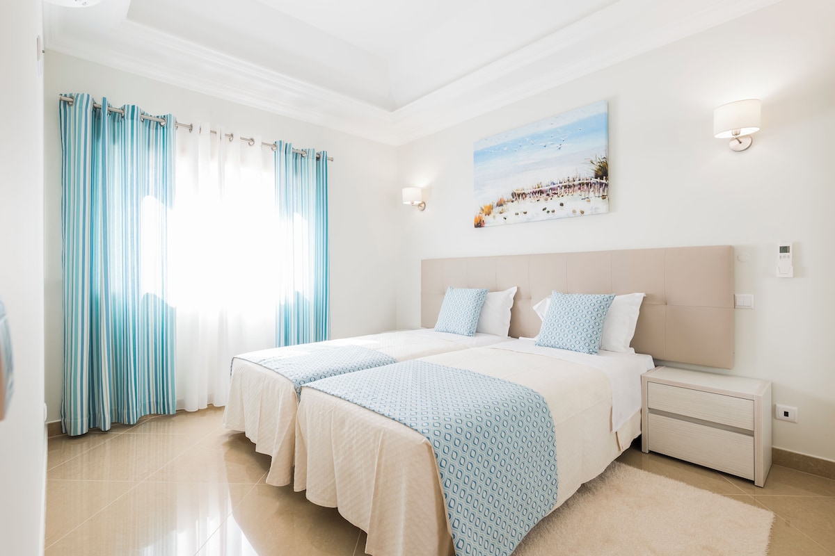 A hotel room with a large bed, a bedside table, a nightstand, and a painting on the wall.