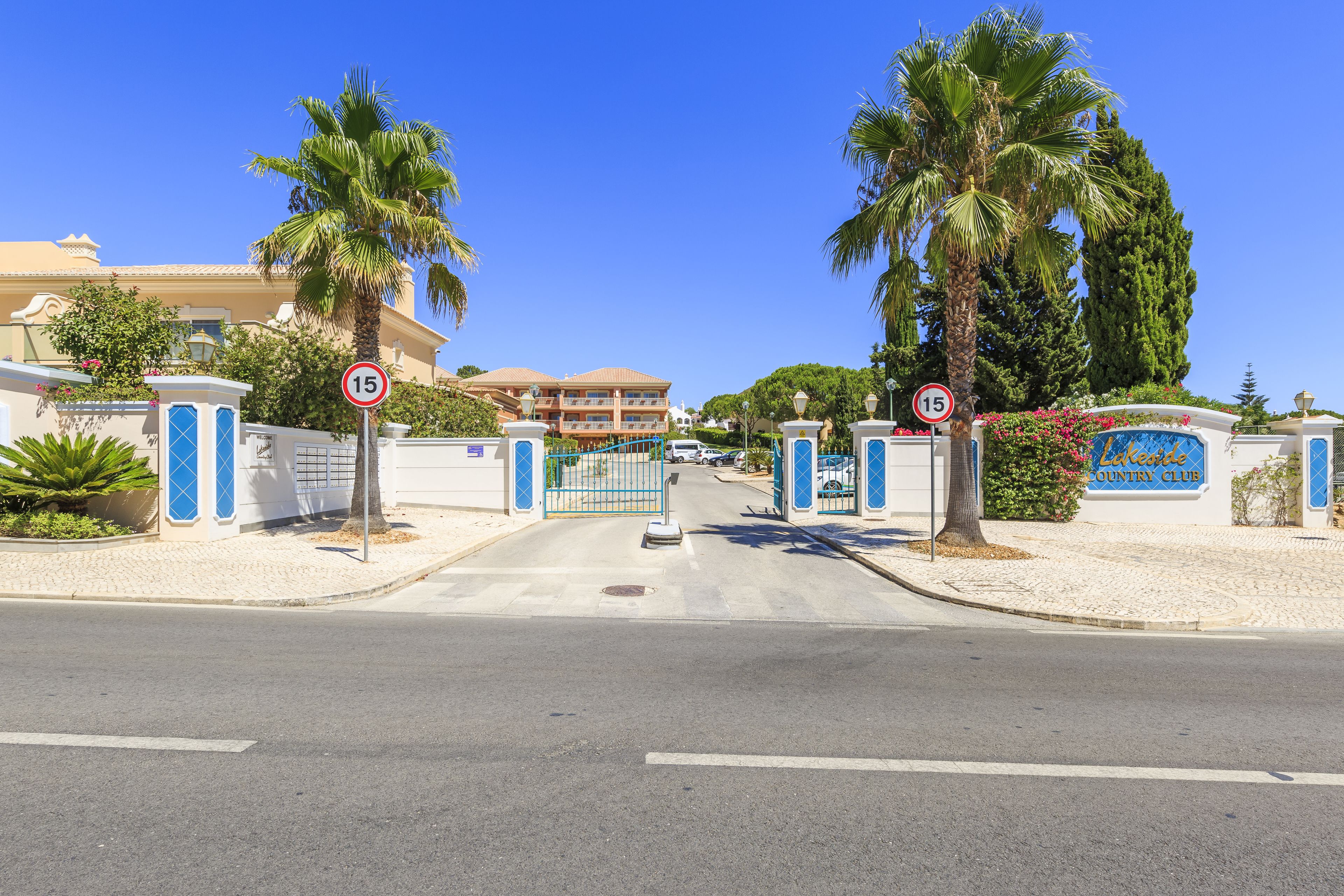 A gated entrance with palm trees, a speed limit sign, and a building with a sign that reads "Le Kerfouci Country Club".