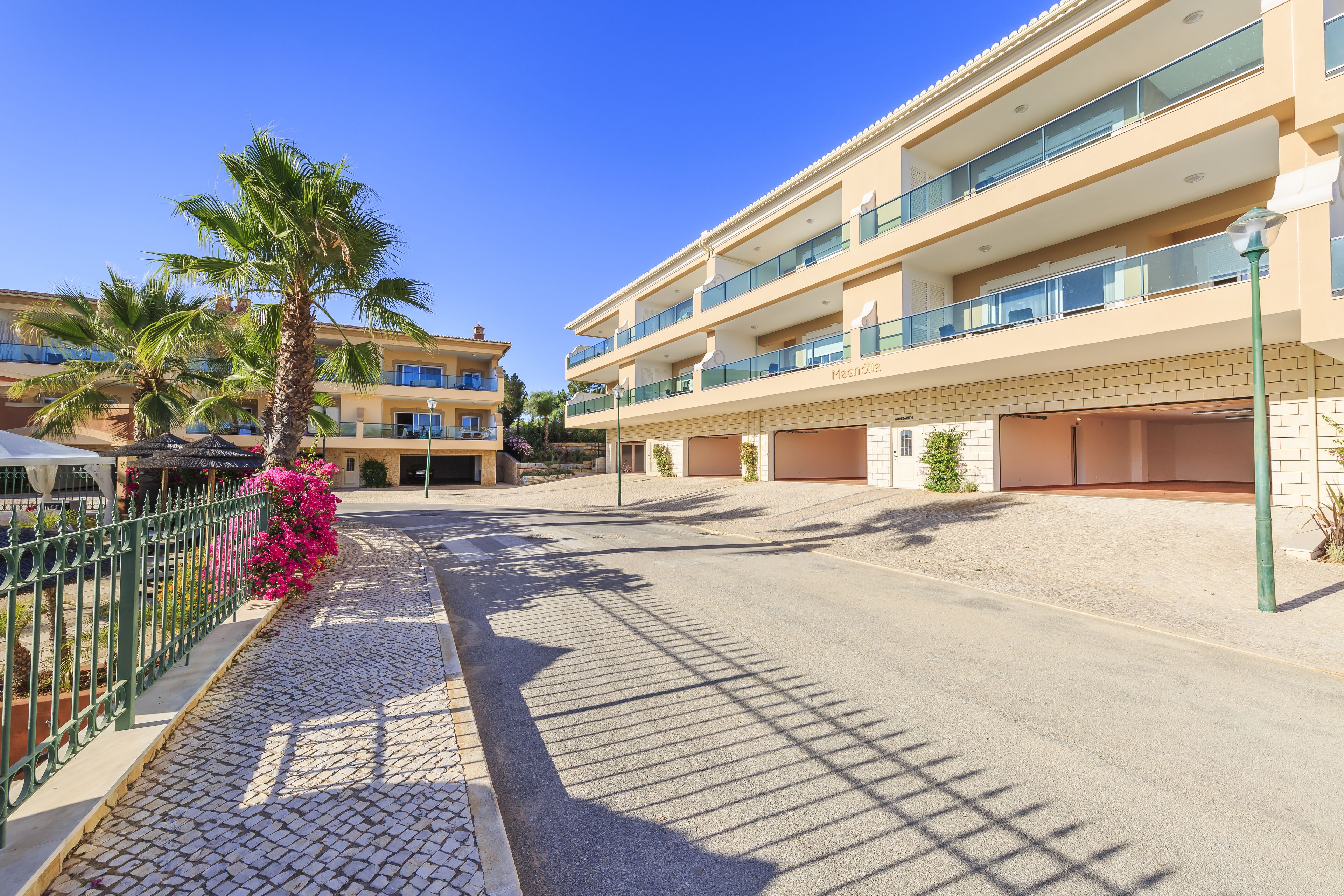 A multi-story hotel with balconies, a paved walkway, and palm trees.