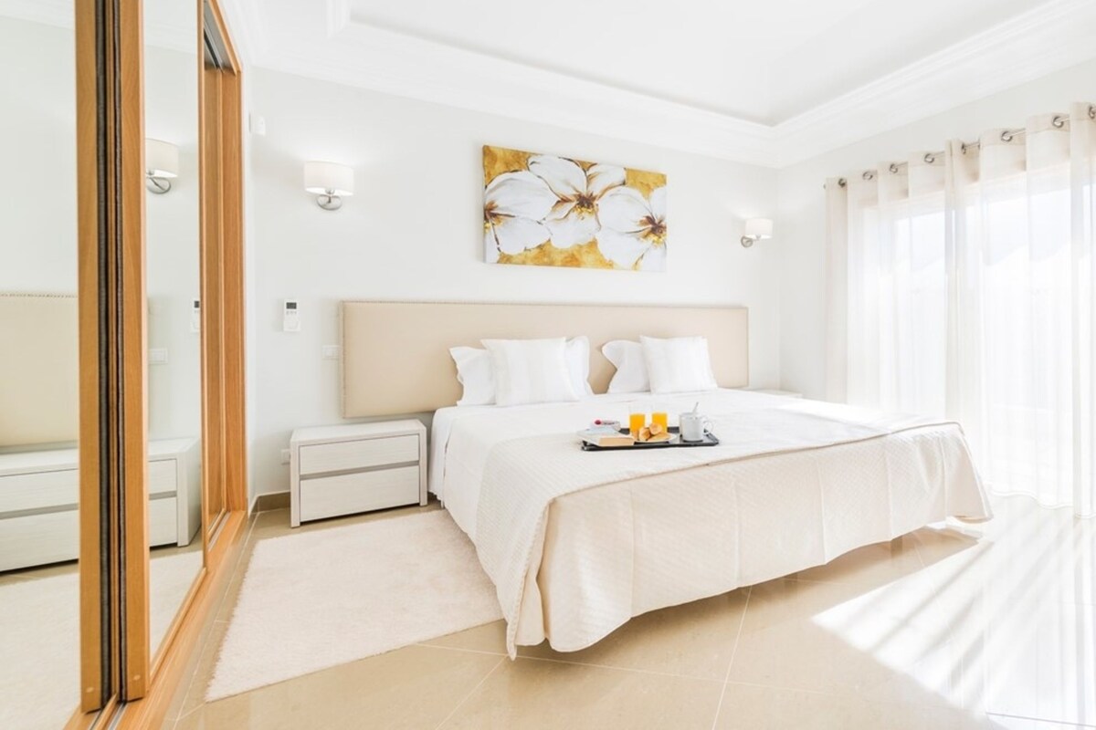 Une chambre d’hôtel avec un grand lit, des tables de chevet, une commode, un miroir et un tableau au mur.