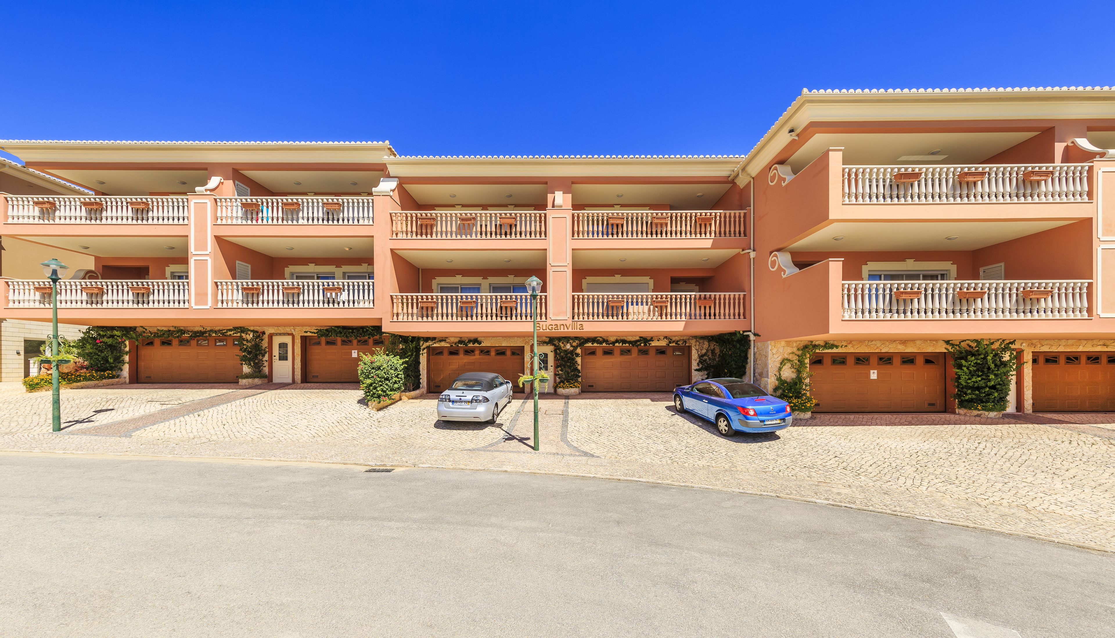 A multi-story hotel with balconies, a paved driveway, and parked cars.