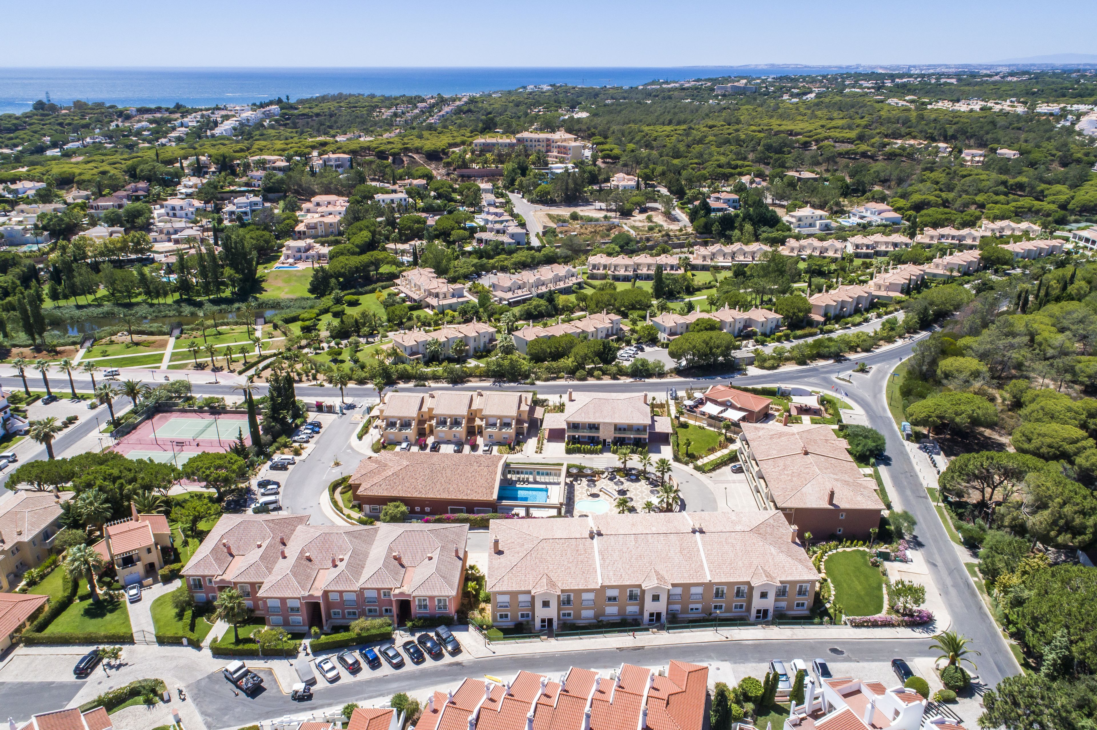 Un quartier résidentiel comprenant un grand immeuble doté de nombreux balcons, d’une piscine et d’un court de tennis.
