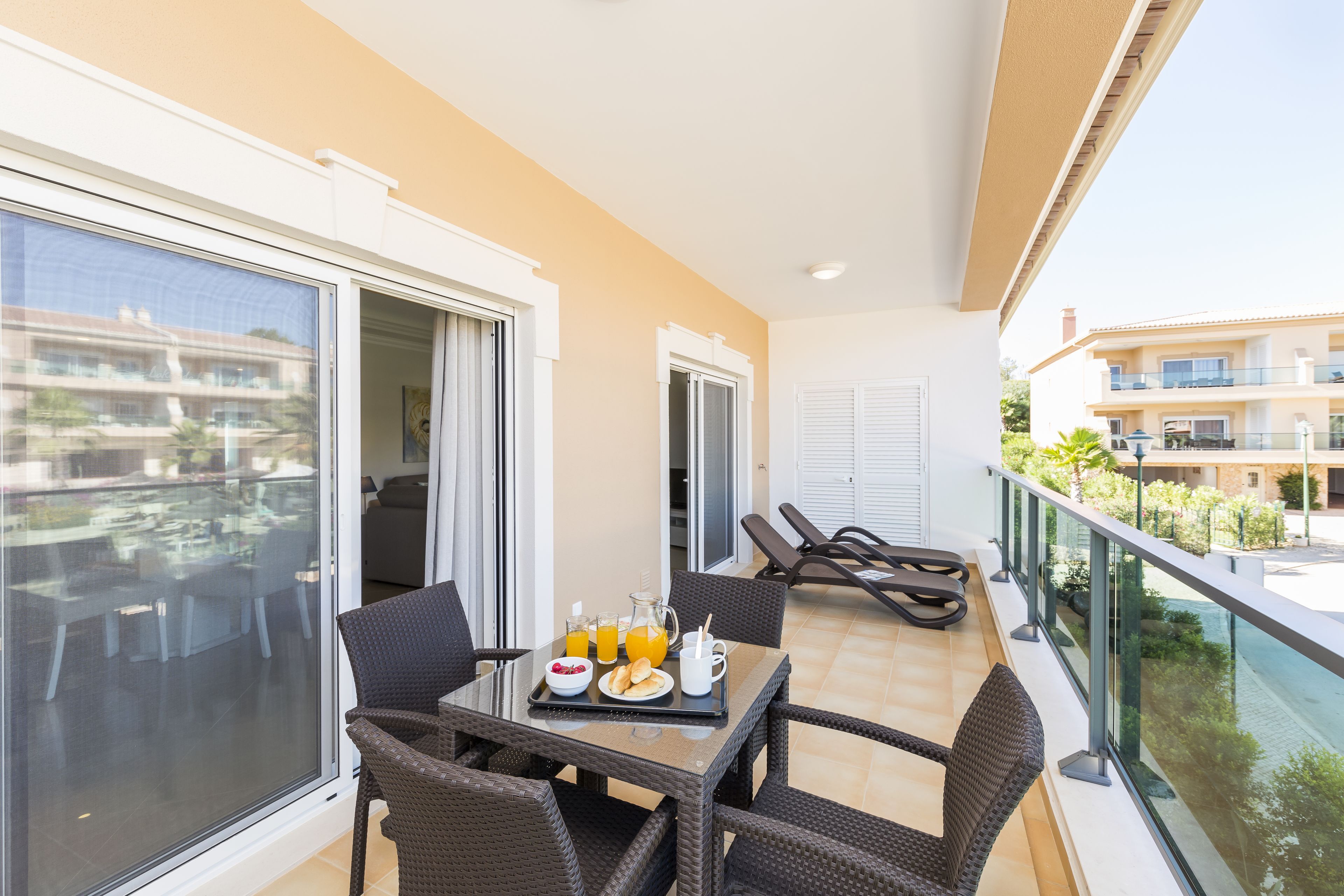 A balcony with a table set for two, two lounge chairs, and a view of the surrounding buildings.