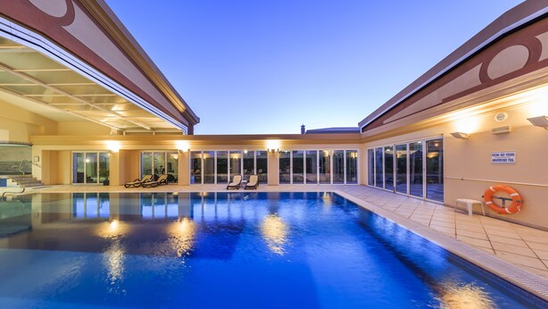 Una piscina interior con paredes de vidrio transparente, un flotador salvavidas y un letrero que indica que la piscina está supervisada.