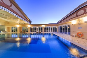 Una piscina interior con paredes de vidrio transparente, un flotador salvavidas y un letrero que indica que la piscina está supervisada.