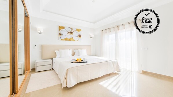 Habitación de hotel con cama, mesitas de noche, espejo, un cuadro y ventana con cortinas.