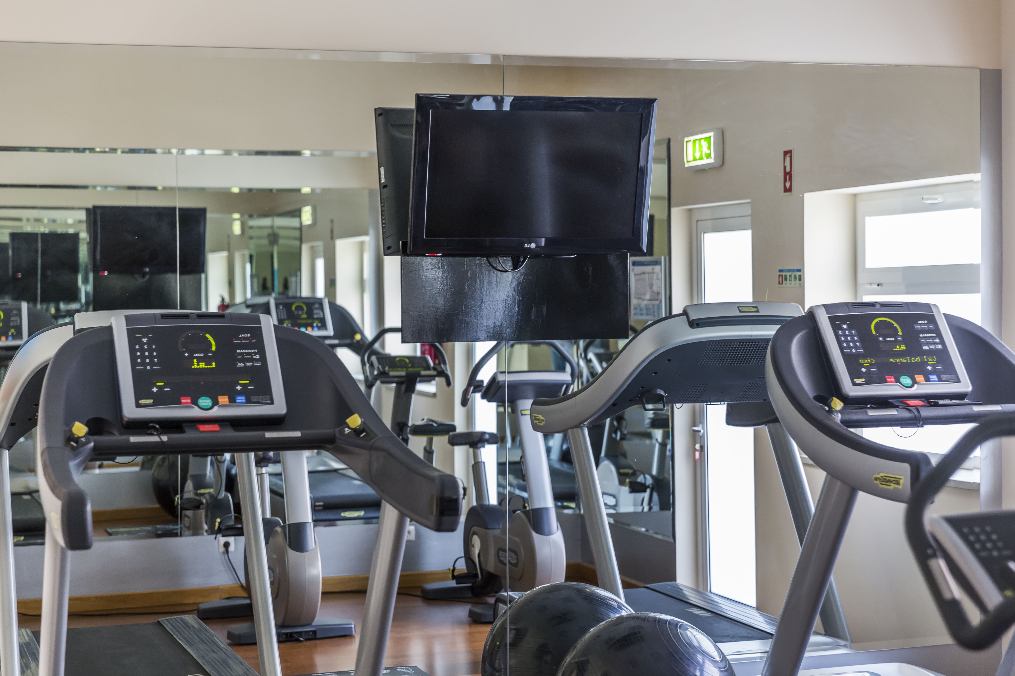 A gym with treadmills, exercise bikes, and a mirrored wall.