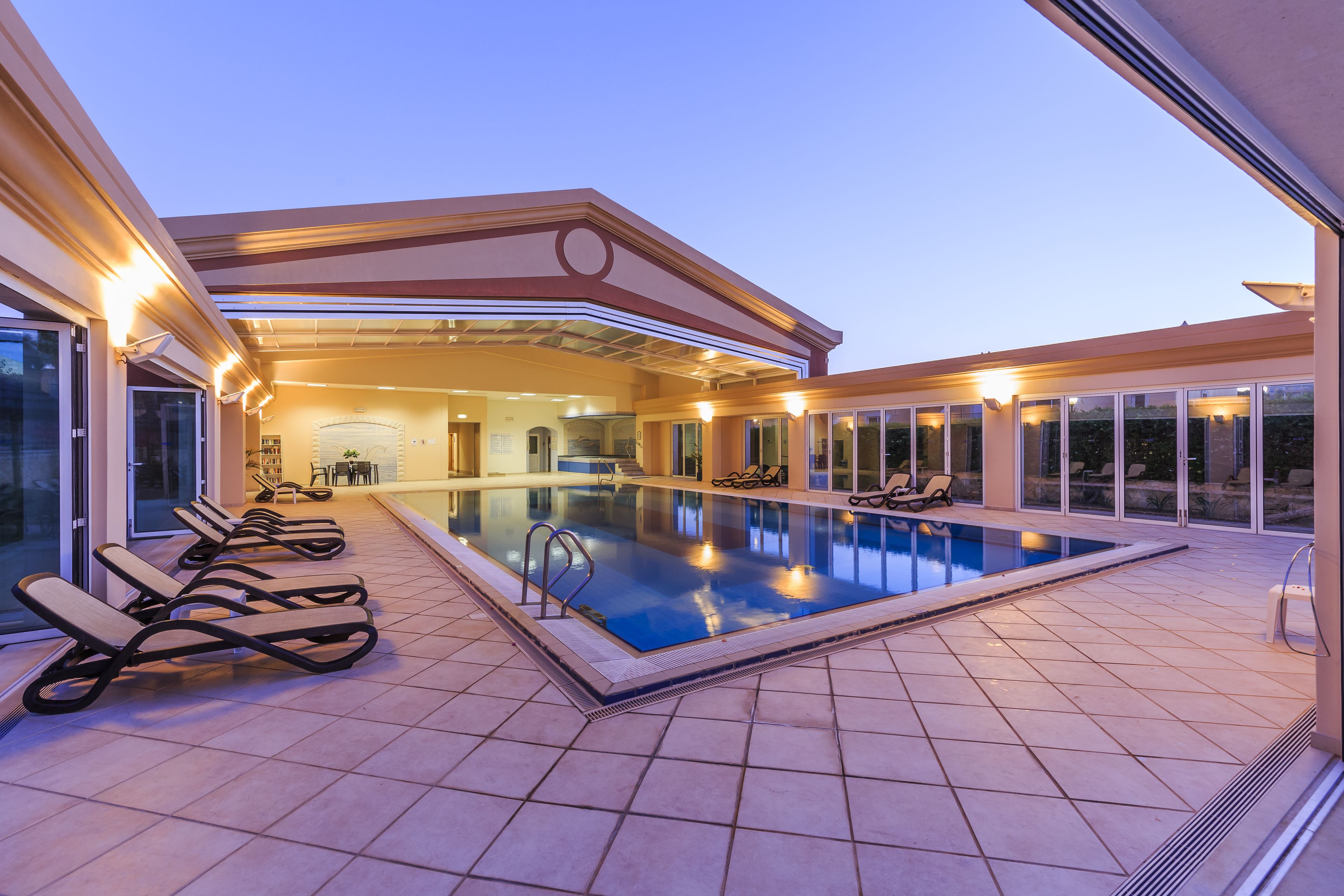 A swimming pool with lounge chairs and a covered area with a view of the interior.