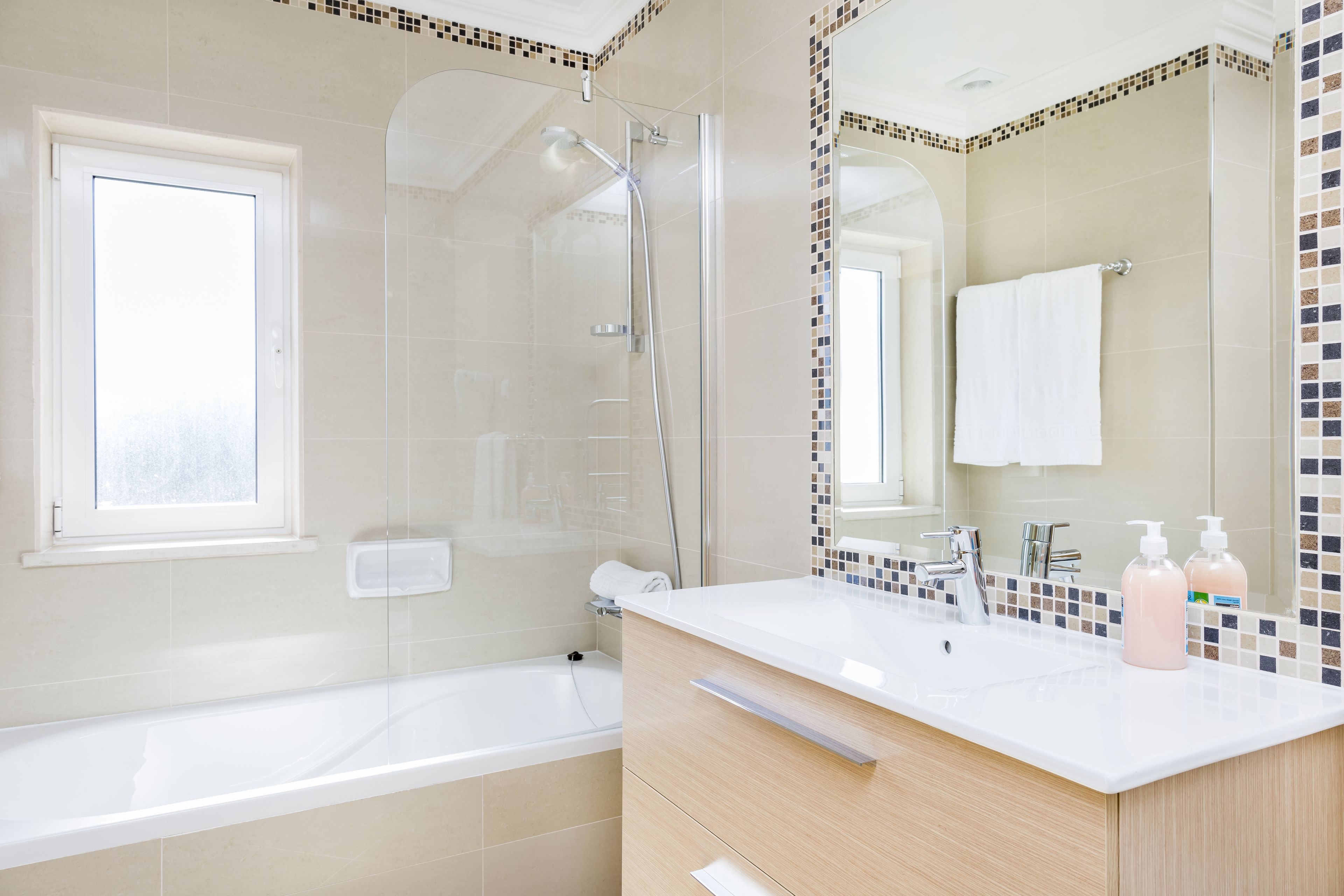 A modern bathroom with a glass-enclosed shower, a white bathtub, and a vanity with a mirror.