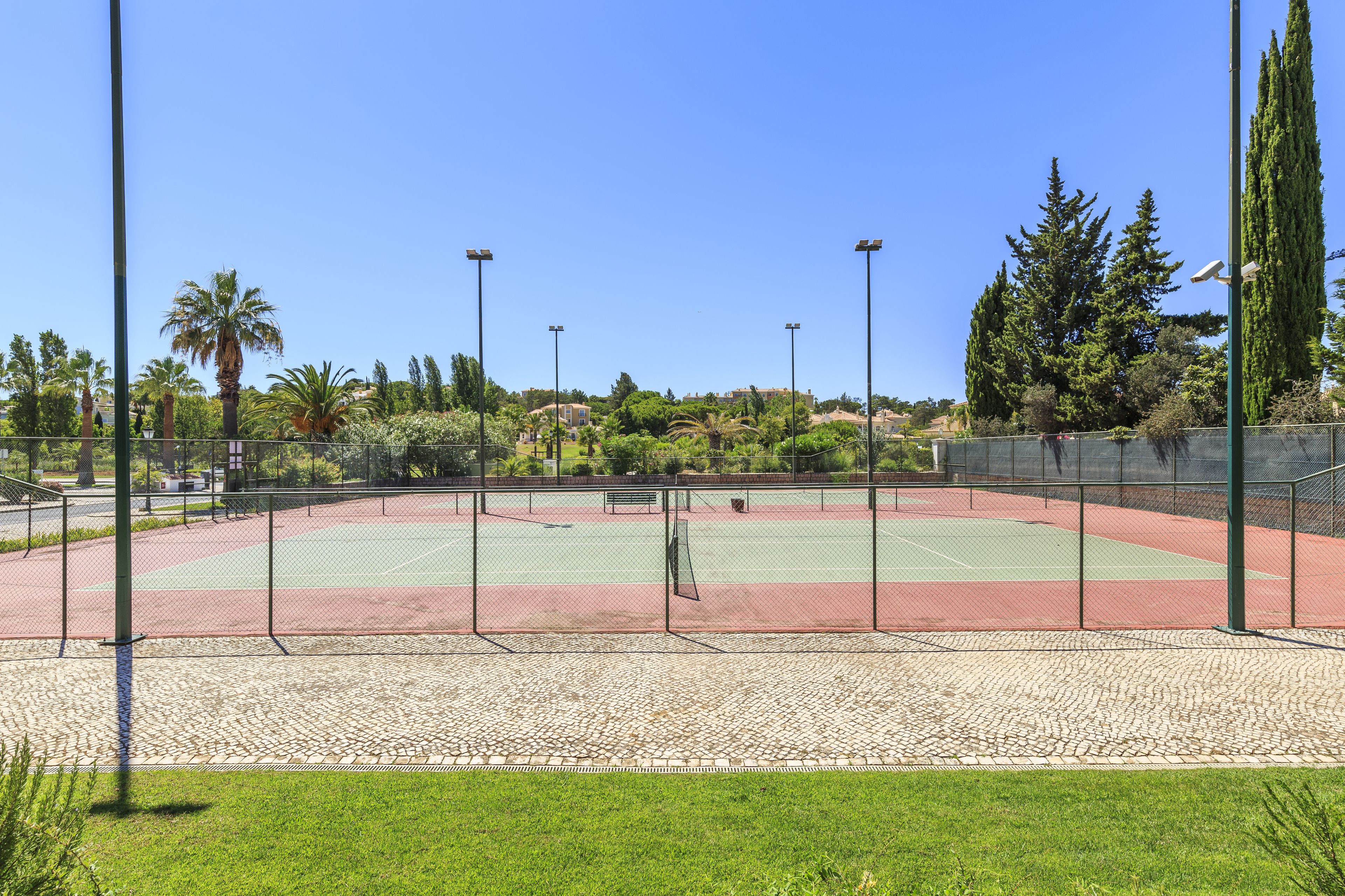 Una cancha de tenis al aire libre con una red, rodeada por una cerca y palmeras.