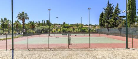 Una cancha de tenis al aire libre con una red, rodeada por una cerca y palmeras.