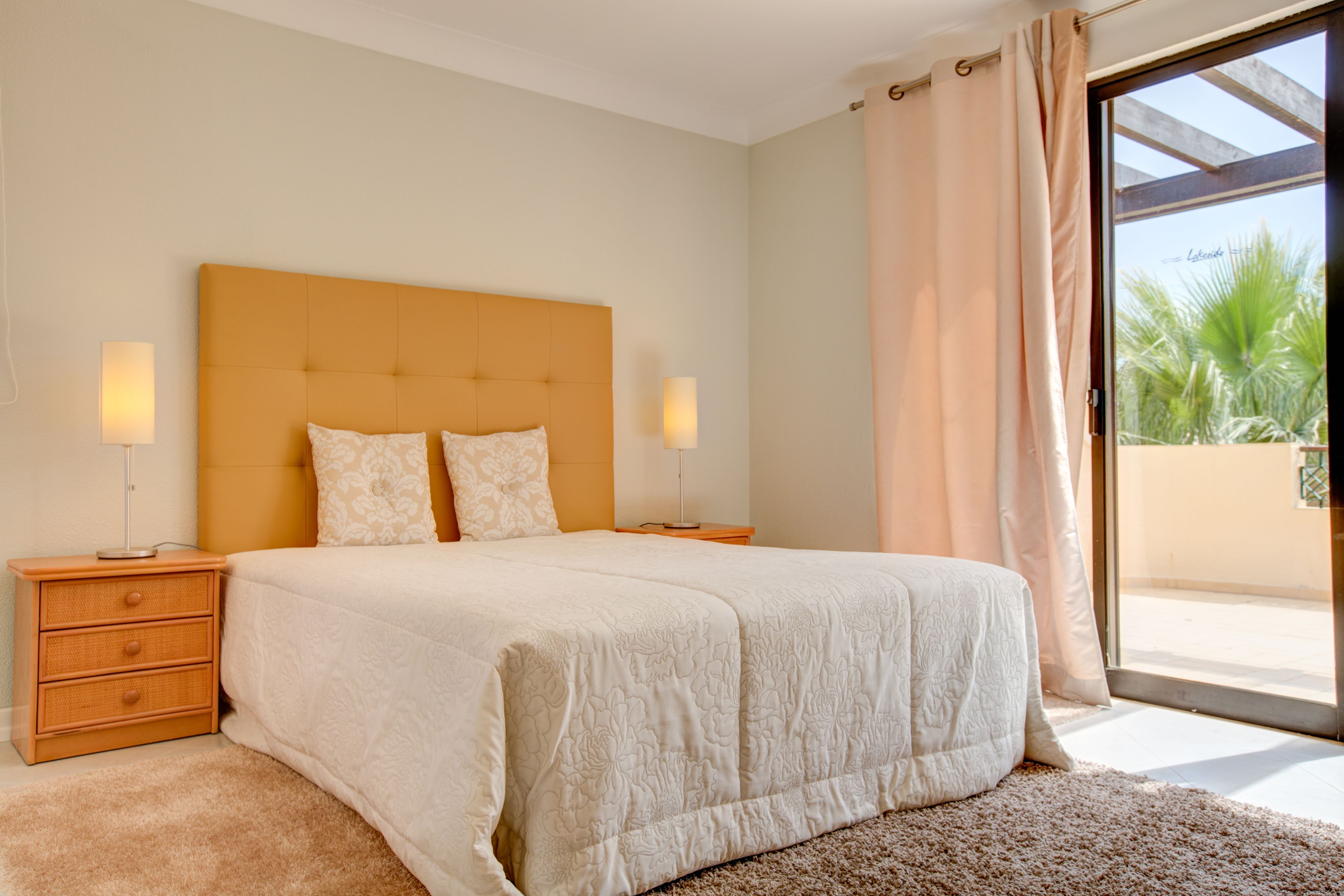 Une chambre avec un grand lit, deux tables de chevet et une vue sur l’extérieur grâce à une porte-fenêtre coulissante.