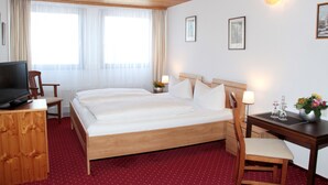Una habitación de hotel con una cama grande, un escritorio, una silla, un televisor y una ventana con cortinas.