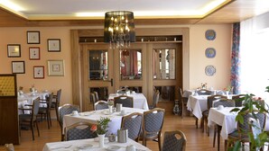 Un comedor con mesas dispuestas para el servicio, sillas y una araña.
