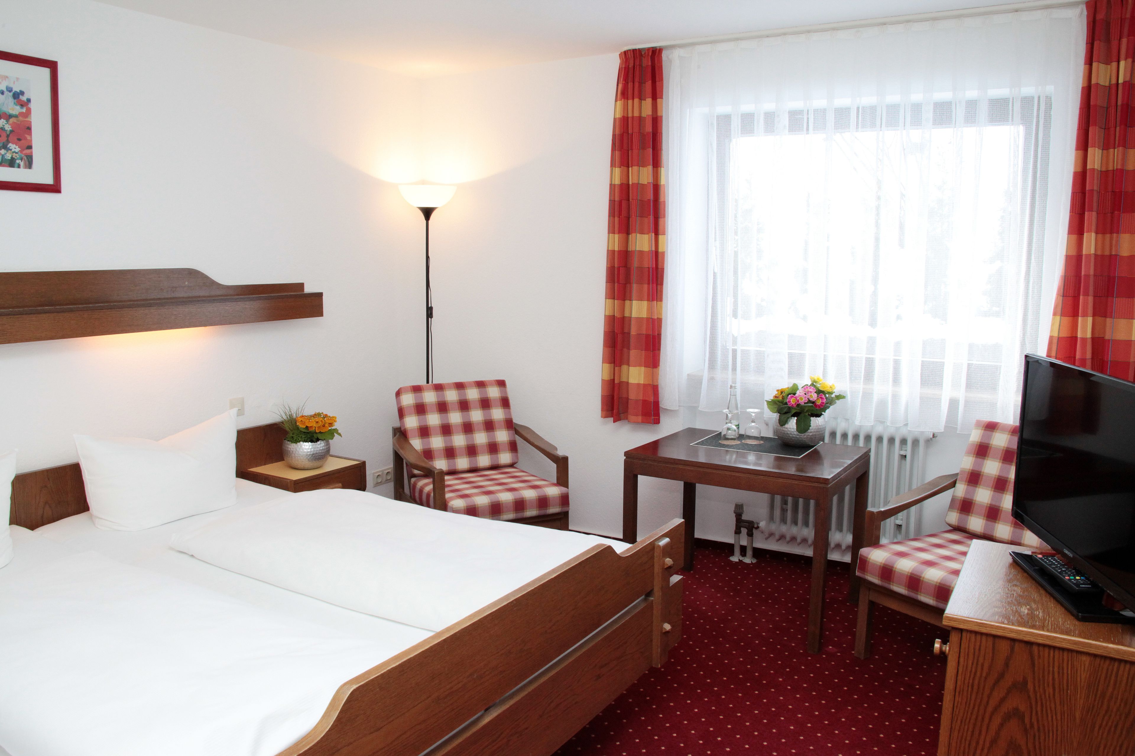 A hotel room with a bed, two chairs, a table, a TV, and a lamp.
