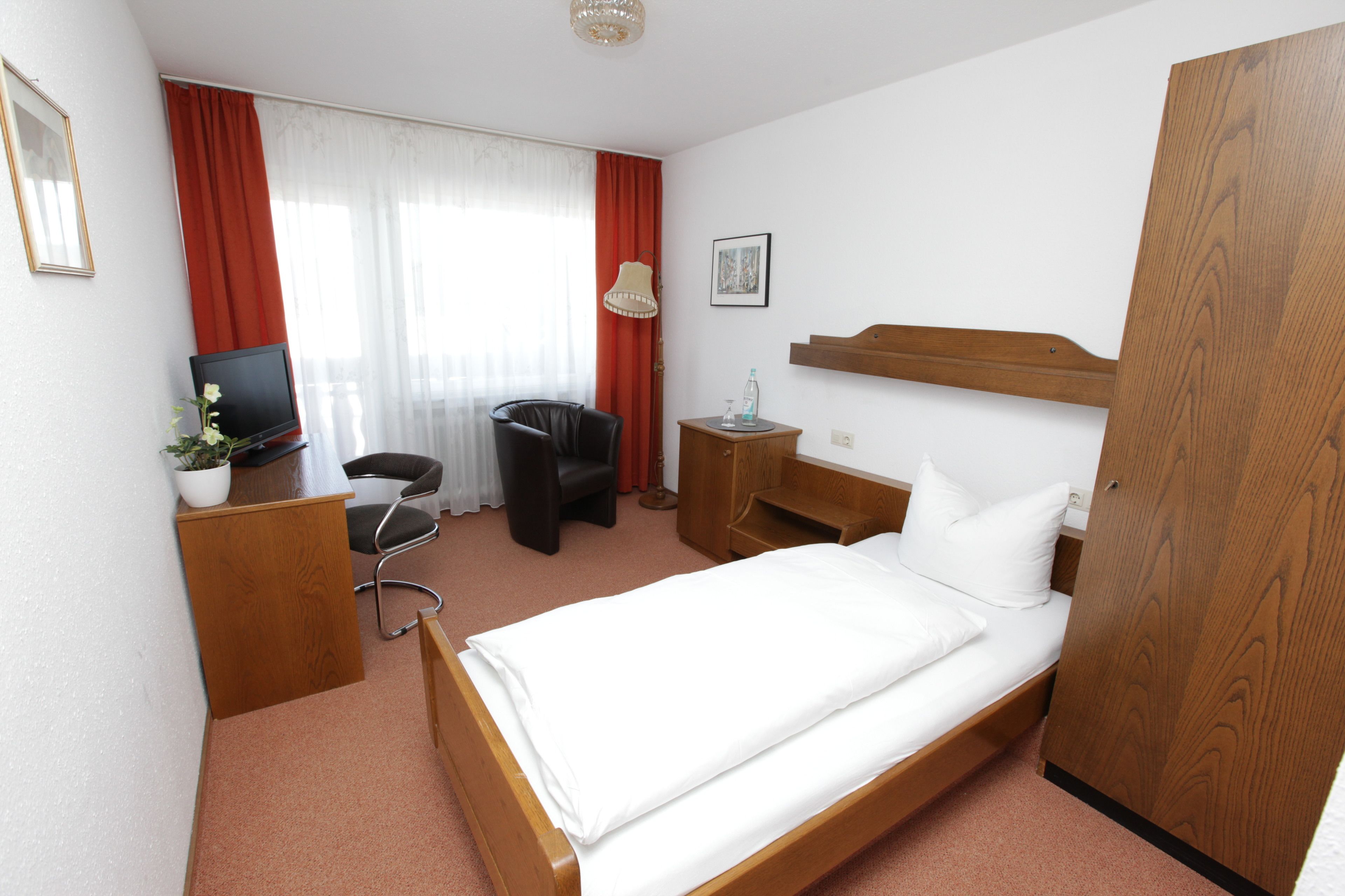 A hotel room with a bed, a desk, a chair, a television, and a window with curtains.