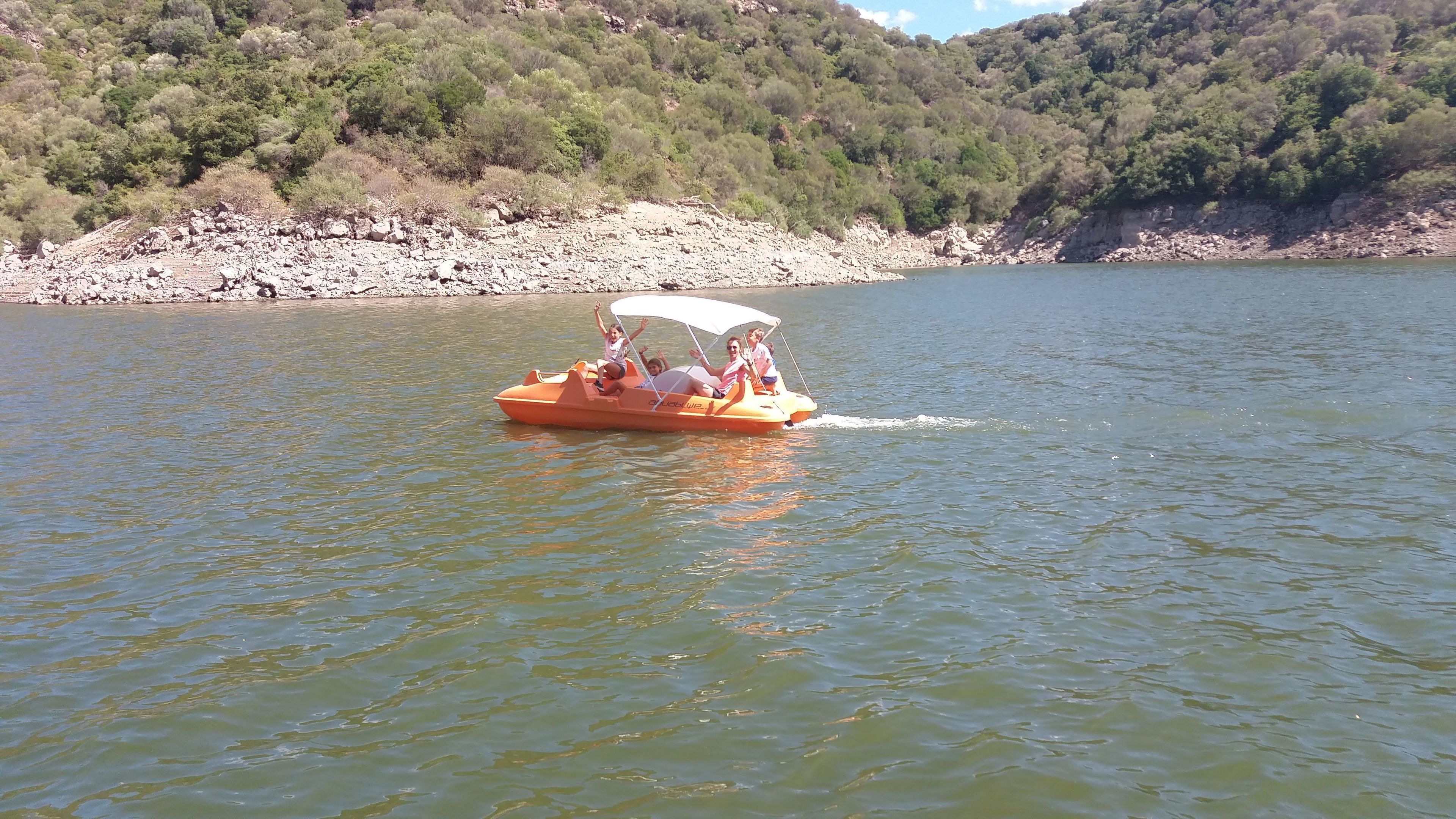 Una pequeña embarcación naranja con toldo, transportando a varias personas, navega en aguas tranquilas.