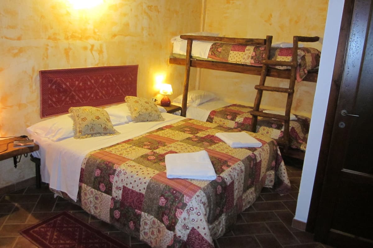 Quarto com duas camas, cabeceira vermelha, escada de madeira e luminária fixada na parede.