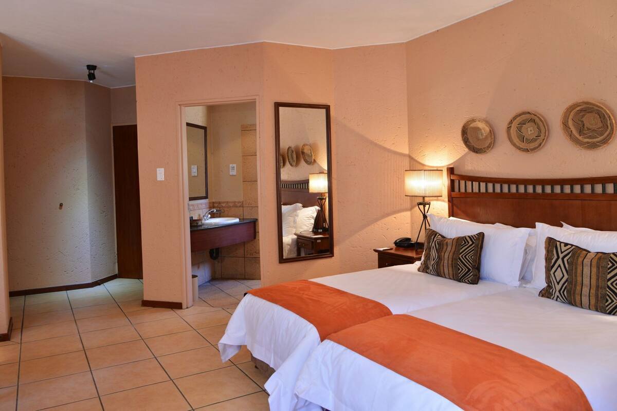 A hotel room with a bed, a nightstand, a lamp, a mirror, and a bathroom visible through an open door.