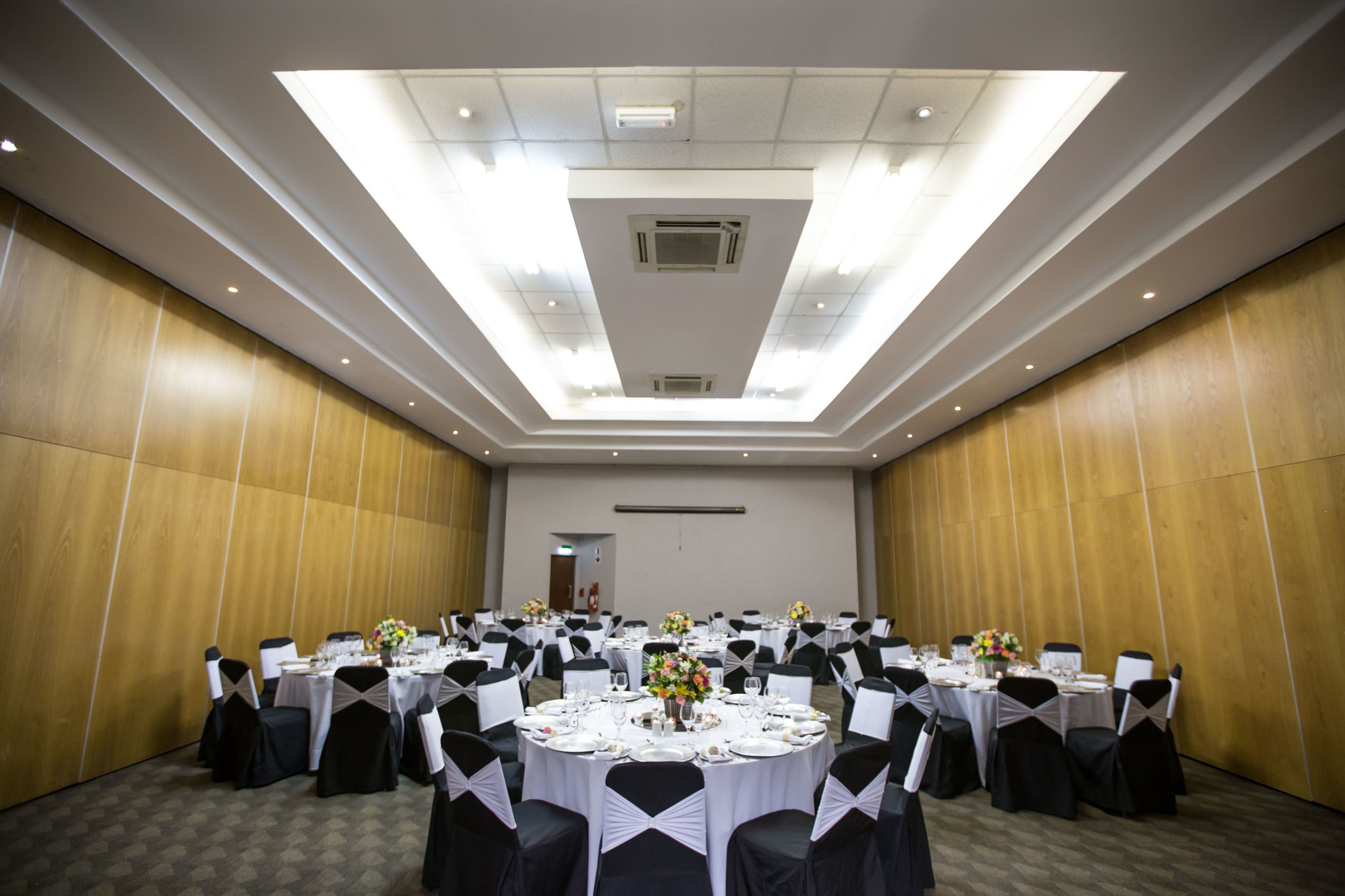 A conference room with round tables, black chairs, and white tablecloths.