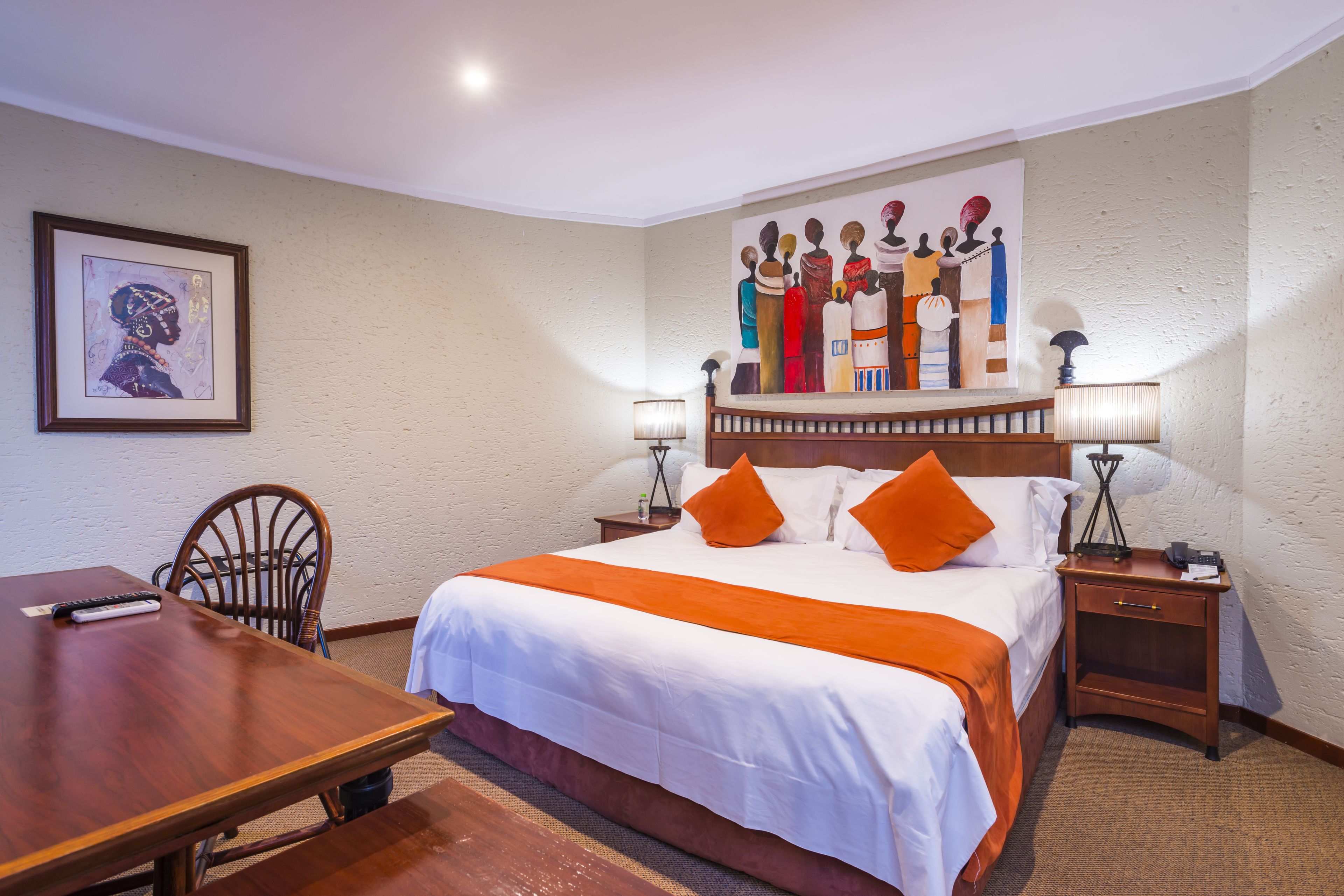 Habitación de hotel con una cama grande, un escritorio y una silla. Hay un cuadro en la pared y una lámpara en la mesita de noche.