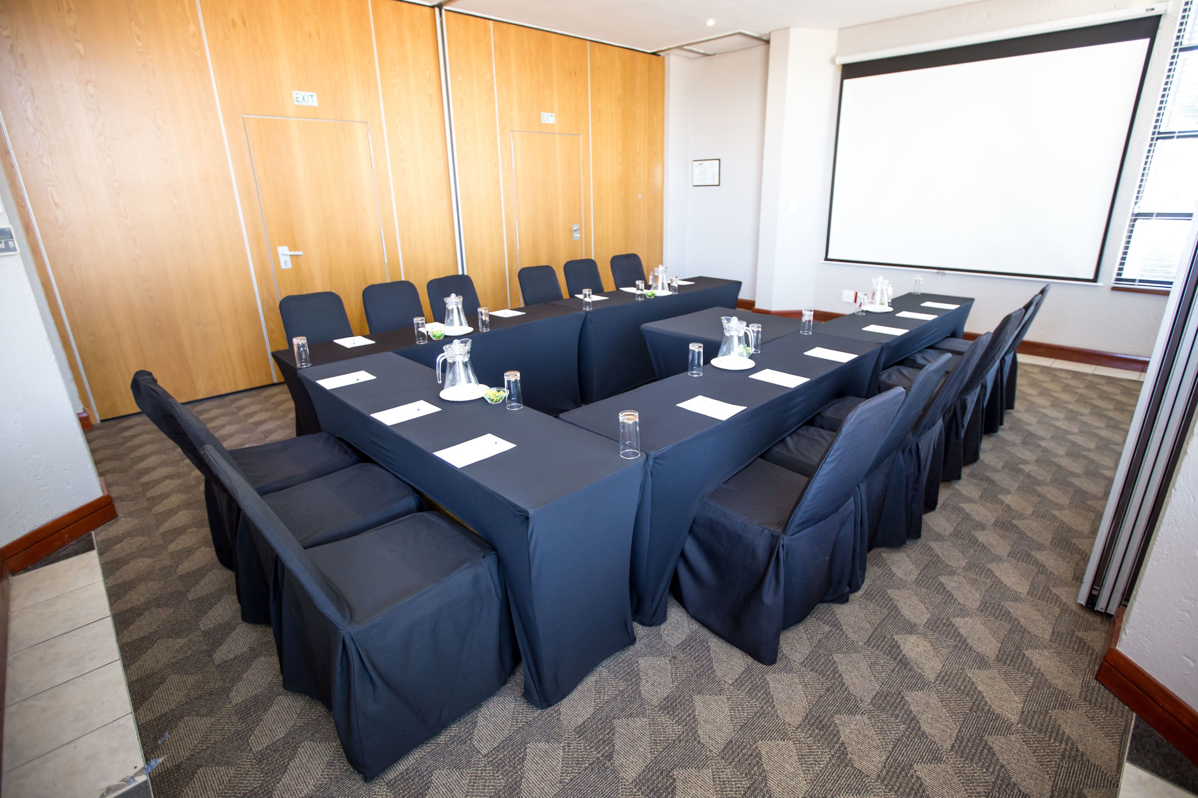 Un salón de conferencias con una larga mesa, sillas y una pantalla para proyector.