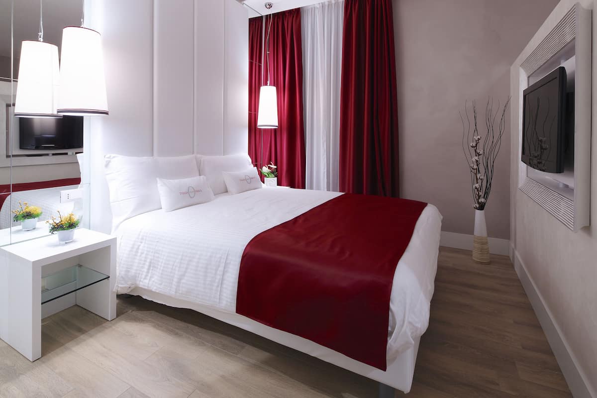 A modern hotel room with a large bed, white nightstands, a flat-screen TV, and a red accent wall.