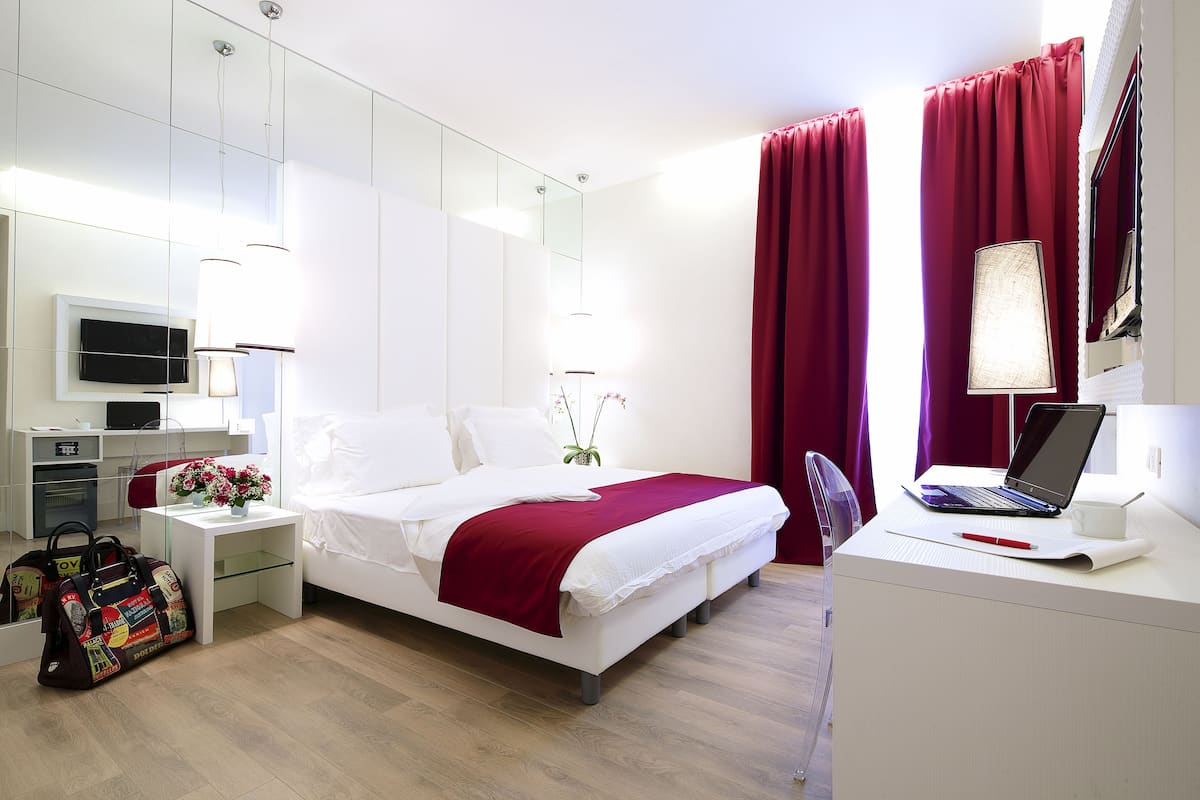A modern hotel room with a bed, desk, and a TV on the wall.