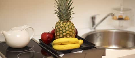 Una encimera de cocina con una tetera blanca, una piña, plátanos y manzanas.