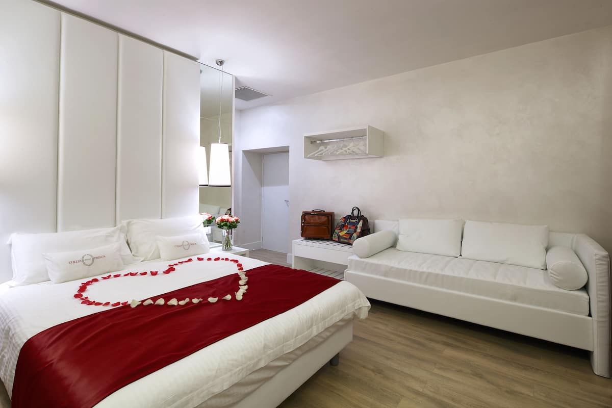 A hotel room with a bed, a white sofa, a nightstand, a mirror, and a wall-mounted shelf.