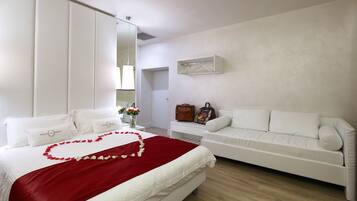 A hotel room with a bed, a white sofa, a nightstand, a mirror, and a wall-mounted shelf.