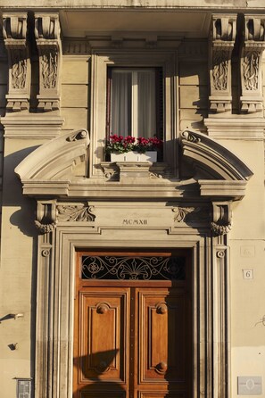 A building facade with a large wooden door, ornate stone carvings, and a window with flowers. - Tullia e Prisca Relais (Rome)