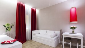 Un salon moderne avec un canapé blanc, une petite table blanche ornée d’un vase de fleurs et un rideau rouge.