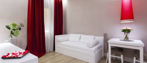 Un salón moderno con un sofá blanco, una mesita pequeña con un jarrón de flores y una cortina roja.